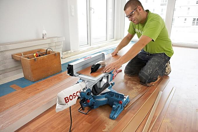 Hombre usando la mesa superior de la ingletadora Bosch GTM 12 JL para cortar un tablón de mafera
